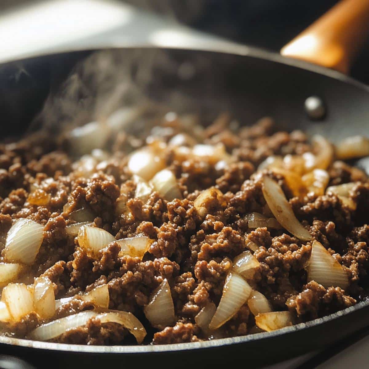 Ground beef and onions cooking in a skillet with slight steam. Shows the savory start of this hearty dish from a home cook’s perspective.