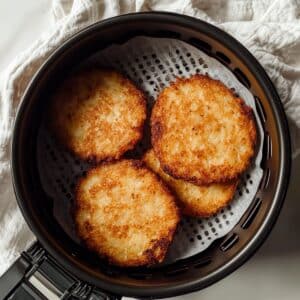 Golden air fryer hash browns in a basket, crisped and ready, shown overhead on a white kitchen counter.