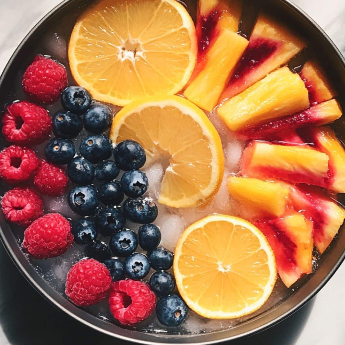A bundt pan filled with water, citrus slices (orange, lemon), berries (blueberries, raspberries), and pineapple chunks is set in a freezer. The ring is clearly forming.