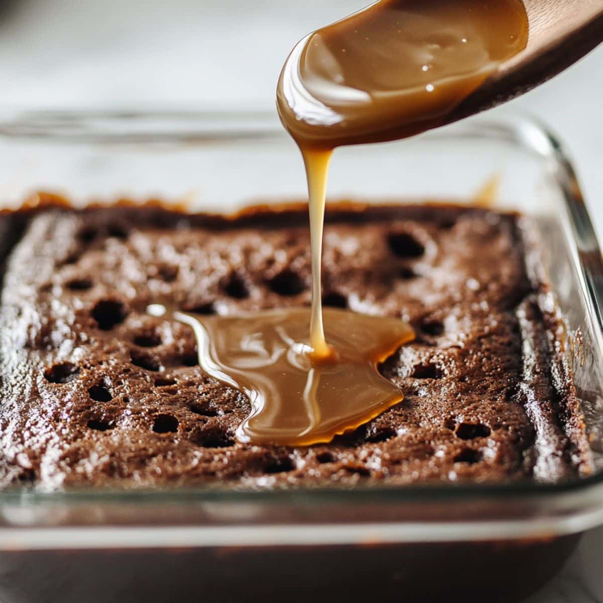 Warm chocolate poke cake in glass pan with holes filled with sweetened condensed milk and caramel sauce. Step-by-step prep of Better Than Anything cake.