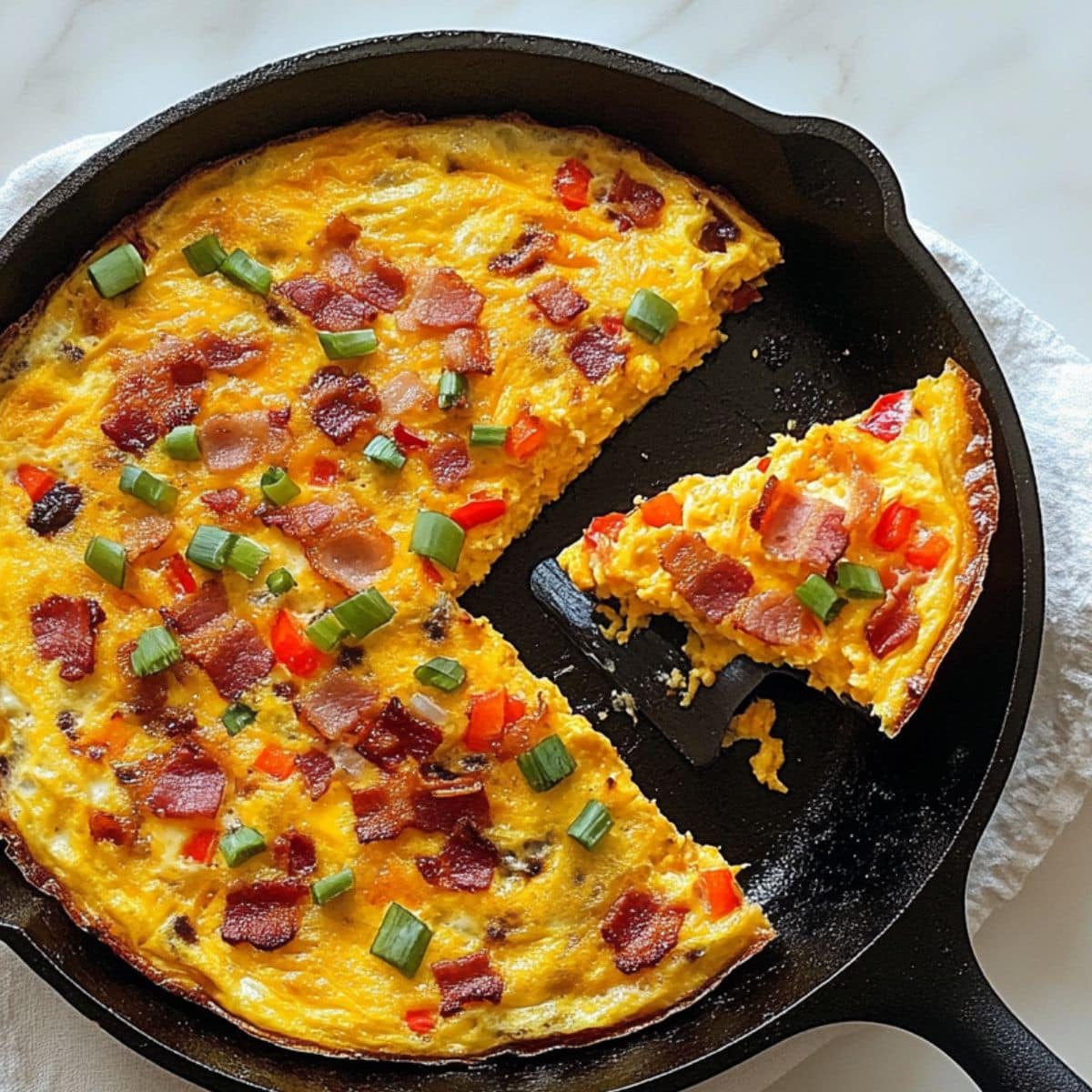 fluffy homemade frittata in a cast iron skillet, topped with crispy bacon, red bell peppers, and green onions, with one slice served.