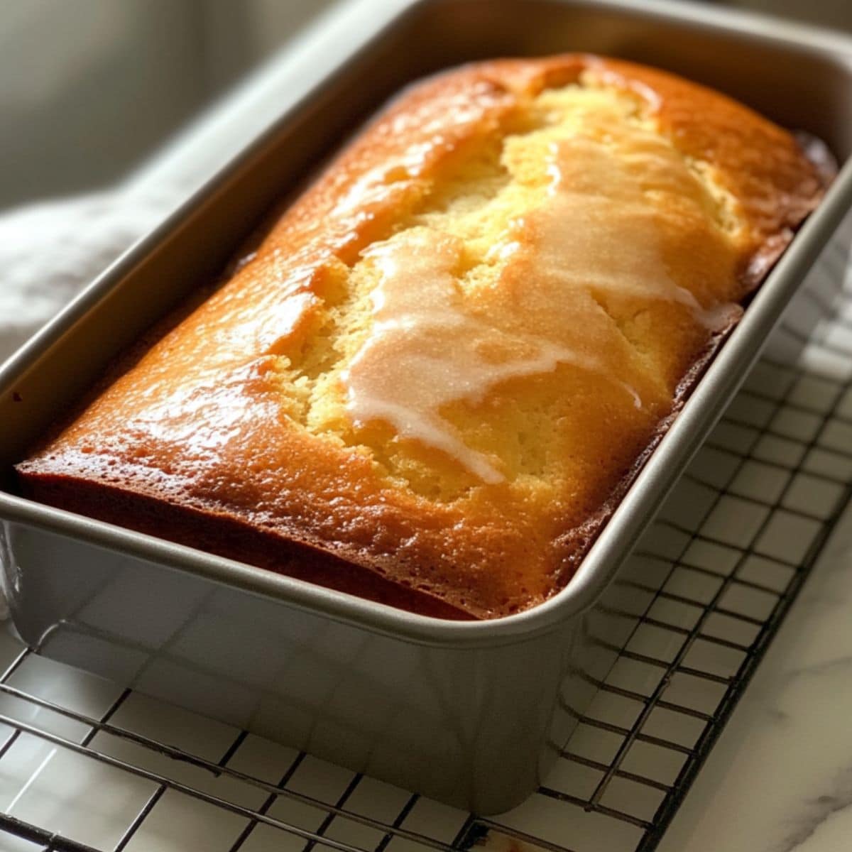 Golden baked lemon pound cake cooling in a pan with a cracked top. Natural lighting with homemade charm and no glaze yet.