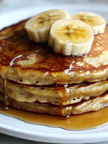 banana pancakes stacked with golden edges, drizzled with maple syrup and fresh banana slices.