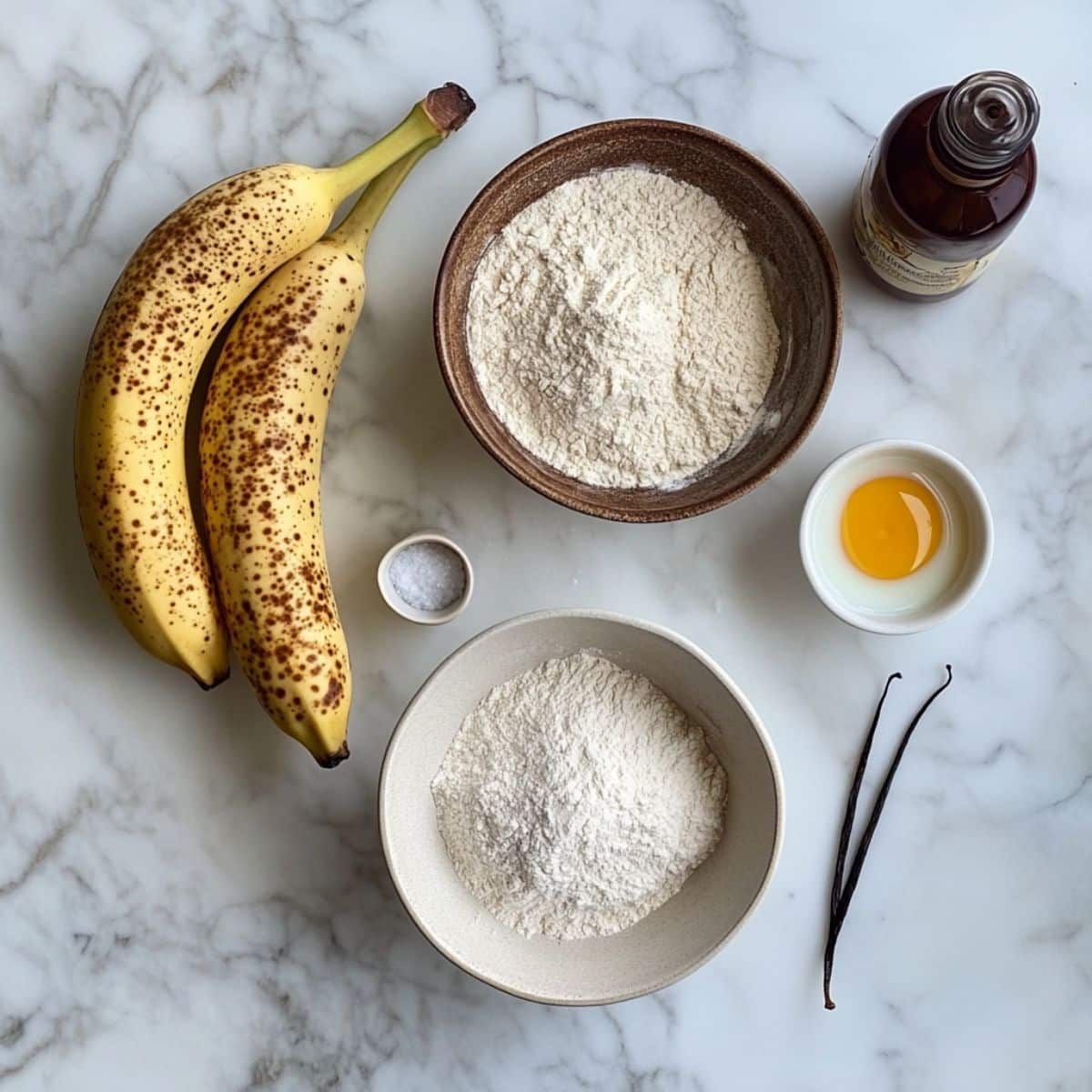 All ingredients for banana pancakes laid out on a white counter. Includes ripe bananas, flour, eggs, milk, yogurt, and optional mix-ins.