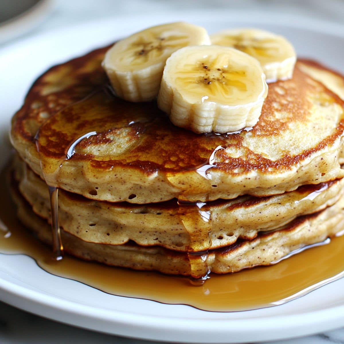 banana pancakes stacked with golden edges, drizzled with maple syrup and fresh banana slices.