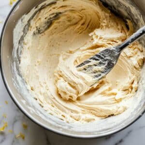 Lemon pound cake batter being gently folded in a bowl with spatula. Smooth texture in a casual home kitchen setting.