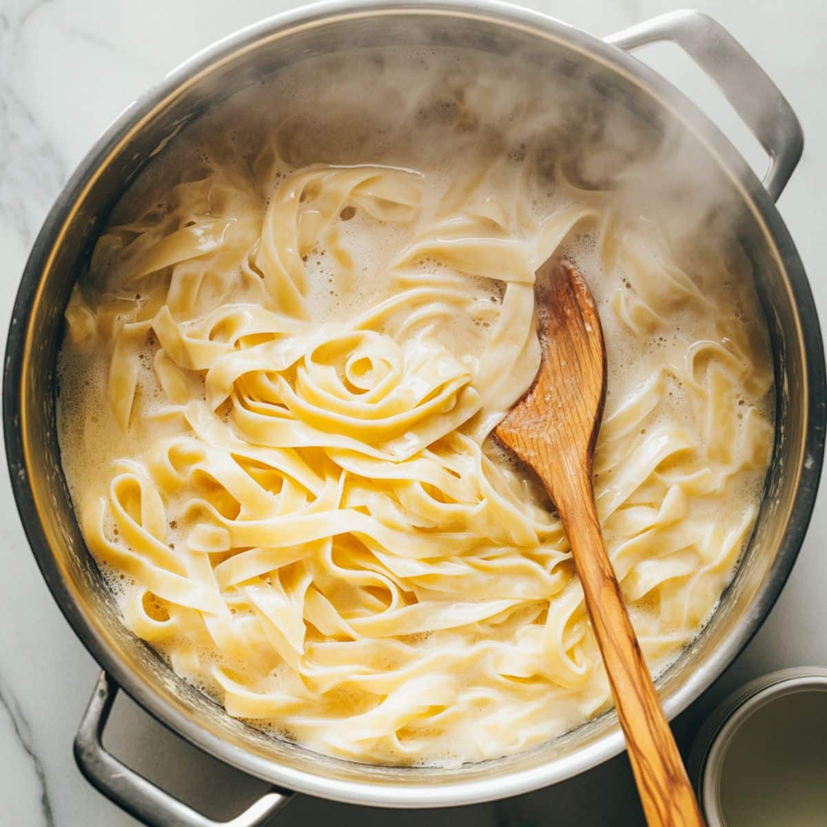 Fettuccine boiling in a pot with steam rising. Pasta water is reserved before draining for creamy shrimp pasta.