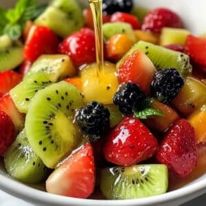Homemade lime and honey dressing being poured over a vibrant fruit salad. Real kitchen prep, no watery mess.