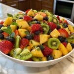 Homemade fruit salad with strawberries, kiwi, pineapple, grapes, melon, and blueberries in a white bowl.