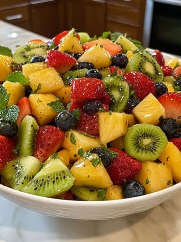 Homemade fruit salad with strawberries, kiwi, pineapple, grapes, melon, and blueberries in a white bowl.
