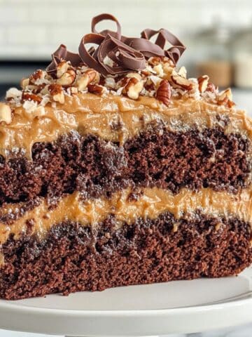 Close-up of a moist German Chocolate Cake slice with caramel coconut pecan frosting and chocolate curls on top.