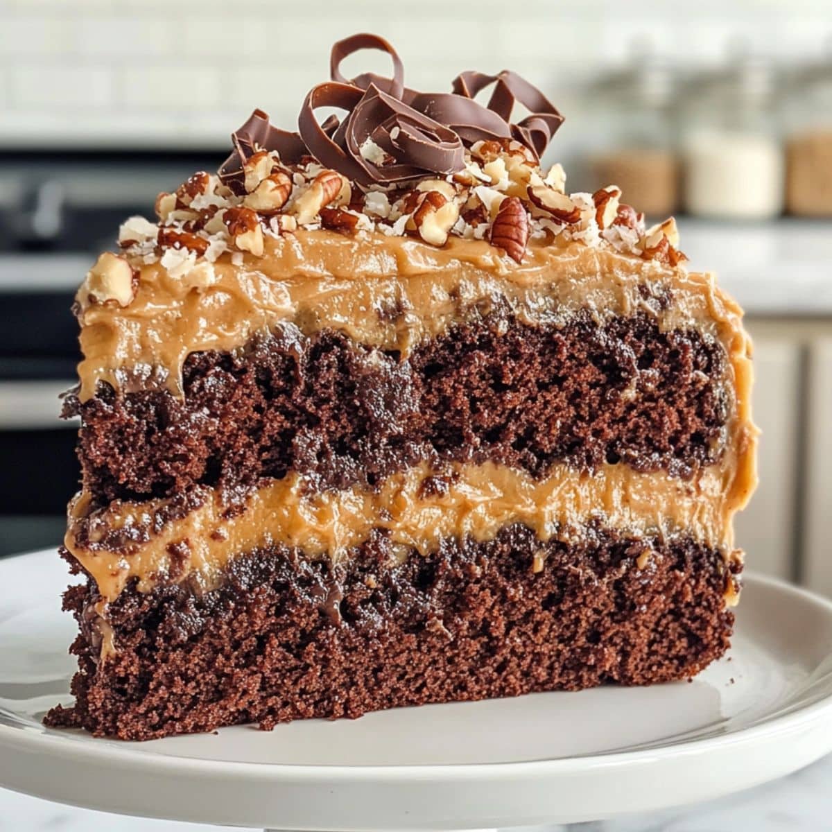 Close-up of a moist German Chocolate Cake slice with caramel coconut pecan frosting and chocolate curls on top.
