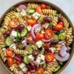 Juicy Greek pasta salad with feta, cucumbers, tomatoes, and olives in a white ceramic bowl.