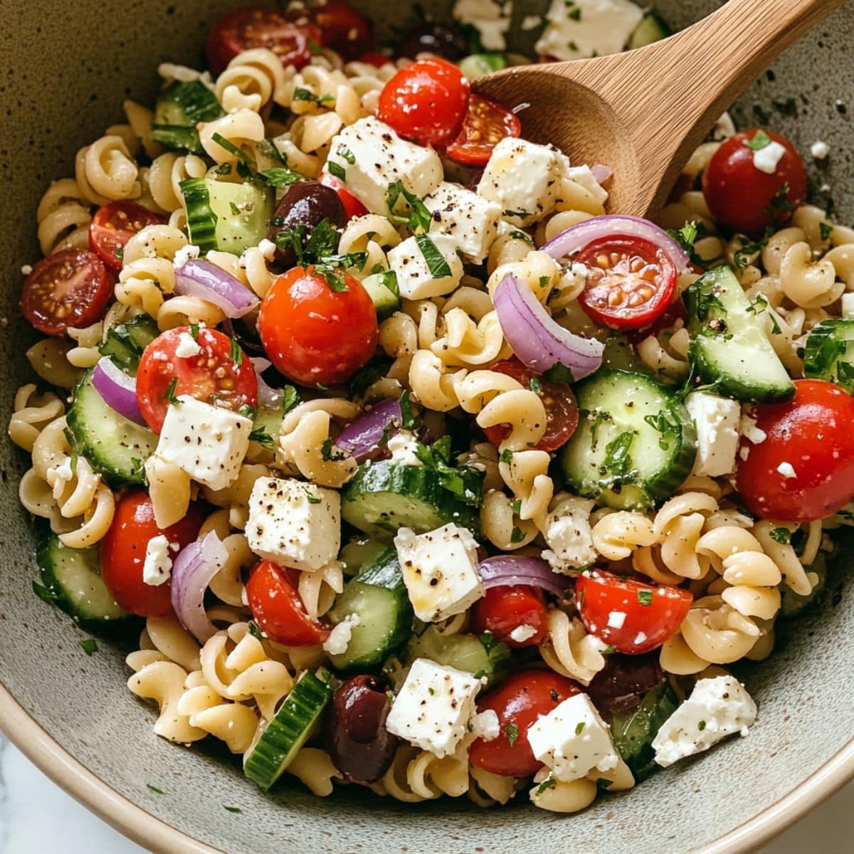 Final mix of Greek pasta salad with dressing, feta, and fresh herbs. A colorful, juicy bowl ready for serving or meal prep.