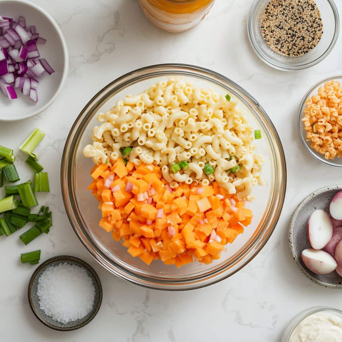 All Hawaiian macaroni salad ingredients on a white counter, including pasta, mayo, eggs, red onion, carrots, and celery in a prep layout.