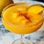 mango margarita in a Tajín-rimmed glass, topped with mango chunks and a fresh mango slice, served thick and slushy.