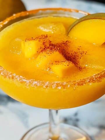 mango margarita in a Tajín-rimmed glass, topped with mango chunks and a fresh mango slice, served thick and slushy.