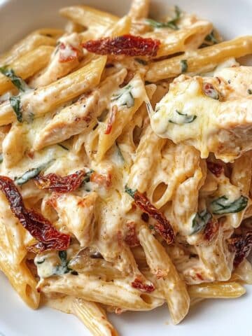 Creamy Marry Me Chicken Pasta with penne, sun-dried tomatoes, basil, and melted mozzarella. Rich, cheesy, and homemade on a white plate.