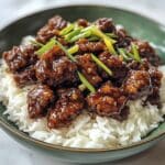 Overhead view of homemade Mongolian beef with rice on a white counter. Glossy sauce and crispy beef pieces give a takeout-style look at home.