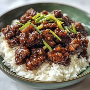 Overhead view of homemade Mongolian beef with rice on a white counter. Glossy sauce and crispy beef pieces give a takeout-style look at home.