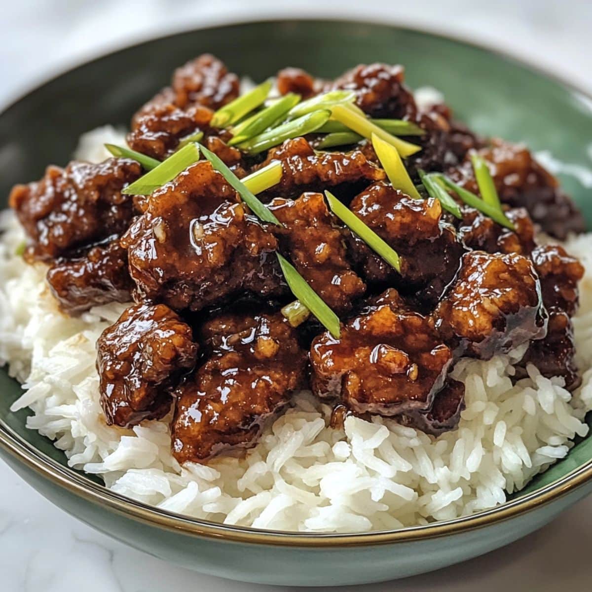 Overhead view of homemade Mongolian beef with rice on a white counter. Glossy sauce and crispy beef pieces give a takeout-style look at home.