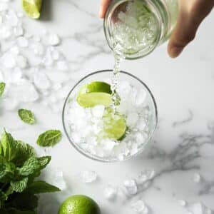 Pouring lime juice into a glass of crushed ice with mint for mojito. Simple homemade drink on kitchen counter.
