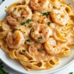 Creamy garlic shrimp pasta on a white plate with parsley and pepper. Real homemade feel with juicy shrimp and fettuccine in rich sauce.