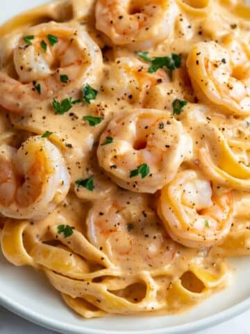 Creamy garlic shrimp pasta on a white plate with parsley and pepper. Real homemade feel with juicy shrimp and fettuccine in rich sauce.
