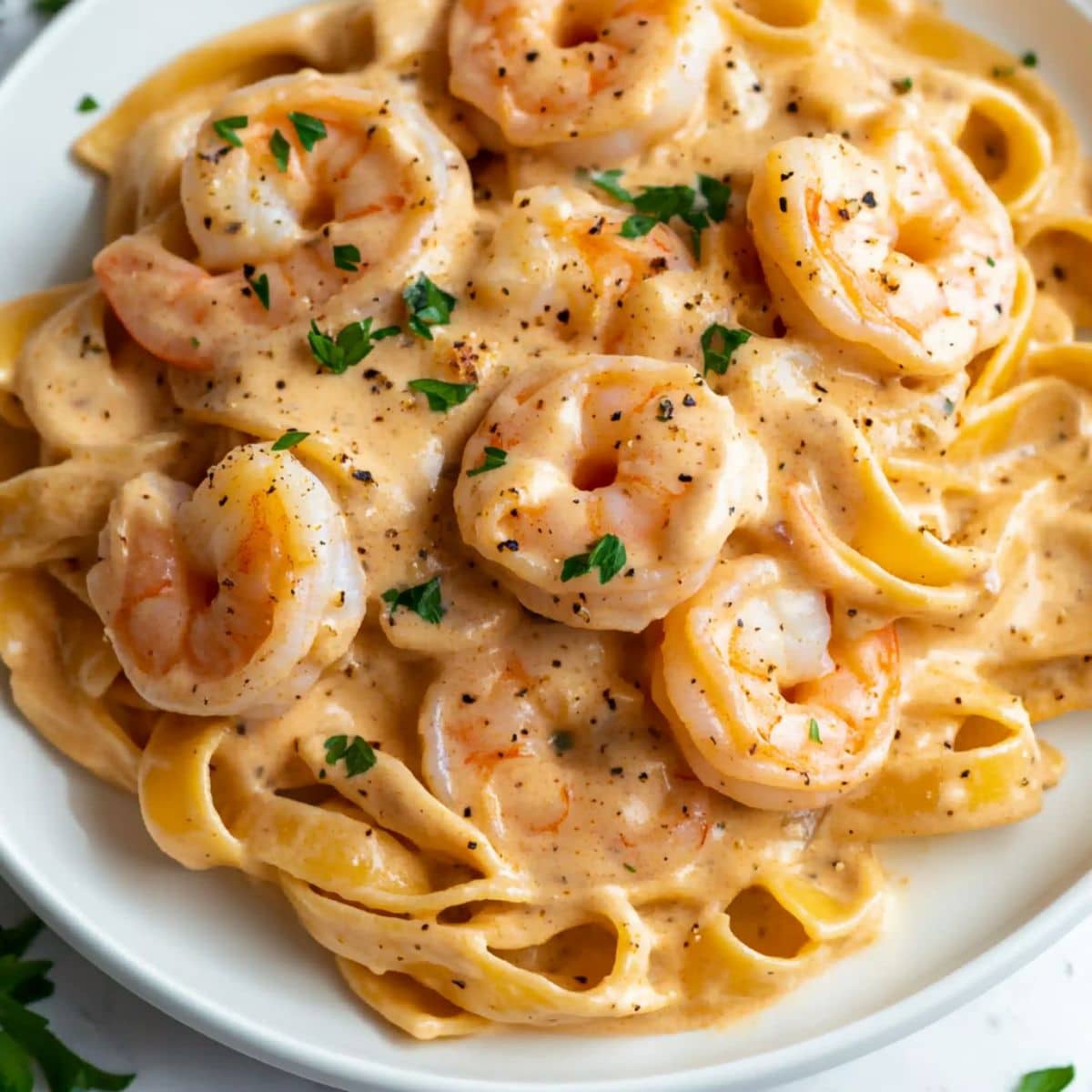 Creamy garlic shrimp pasta on a white plate with parsley and pepper. Real homemade feel with juicy shrimp and fettuccine in rich sauce.