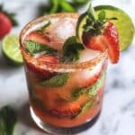 Glass of strawberry mojito with fresh mint, lime, and strawberries.