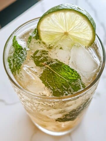 Close-up of virgin mojito with mint, lime slice, and ice cubes in a glass. Fizzy bubbles and fresh herbs on a white marble kitchen counter.