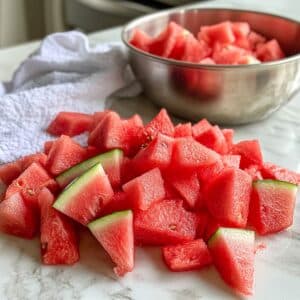 Chilled watermelon chunks prepped for juice on a white kitchen counter. Cold fruit makes smoother, sweeter juice.