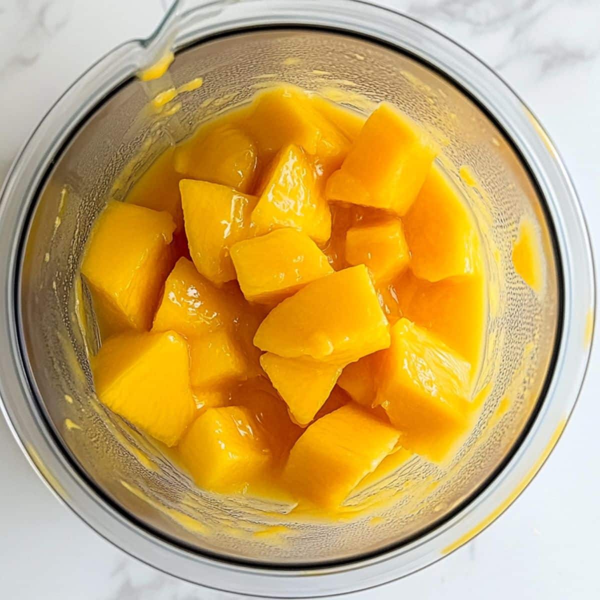 Mango chunks blending into golden puree for sorbet. Natural, homemade process on a white kitchen surface.