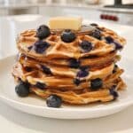 Fluffy golden blueberry waffles stacked high with syrup dripping down the edges.