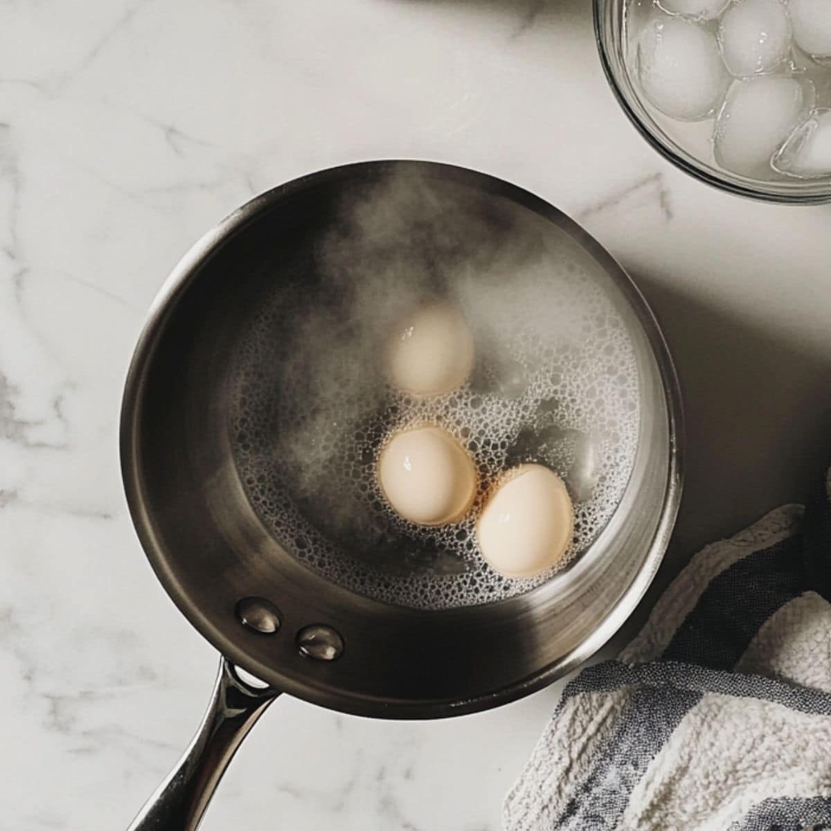Boiling eggs in a saucepan and ice bath nearby for deviled eggs prep. Real kitchen look with casual setup and white counter.