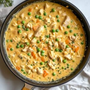 Creamy mixture of chicken, peas, carrots, soup, and spices in skillet ; warm, thick, and ready for baking.