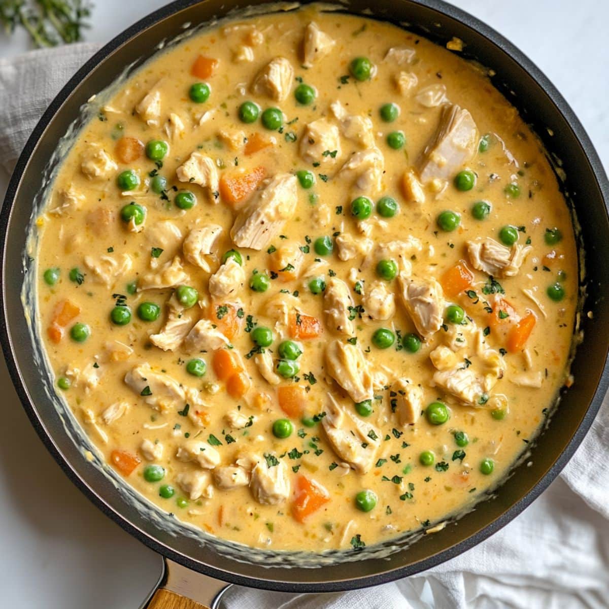 Creamy mixture of chicken, peas, carrots, soup, and spices in skillet ; warm, thick, and ready for baking.