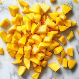 Chopped ripe mango pieces on a board with pit and juice. Prepping mango for homemade sorbet recipe.