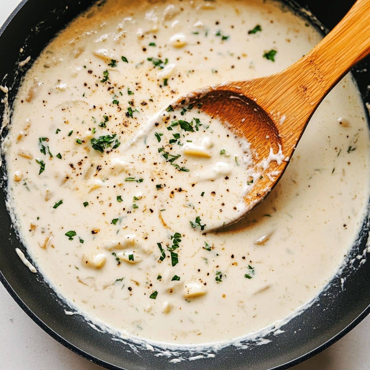 Garlic-Parmesan cream sauce bubbling in skillet. Thick, silky base for shrimp pasta with lemon and herbs.