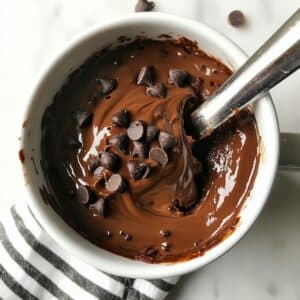 Thick mug cake batter topped with chocolate chips and swirled Nutella, ready to go in the microwave.