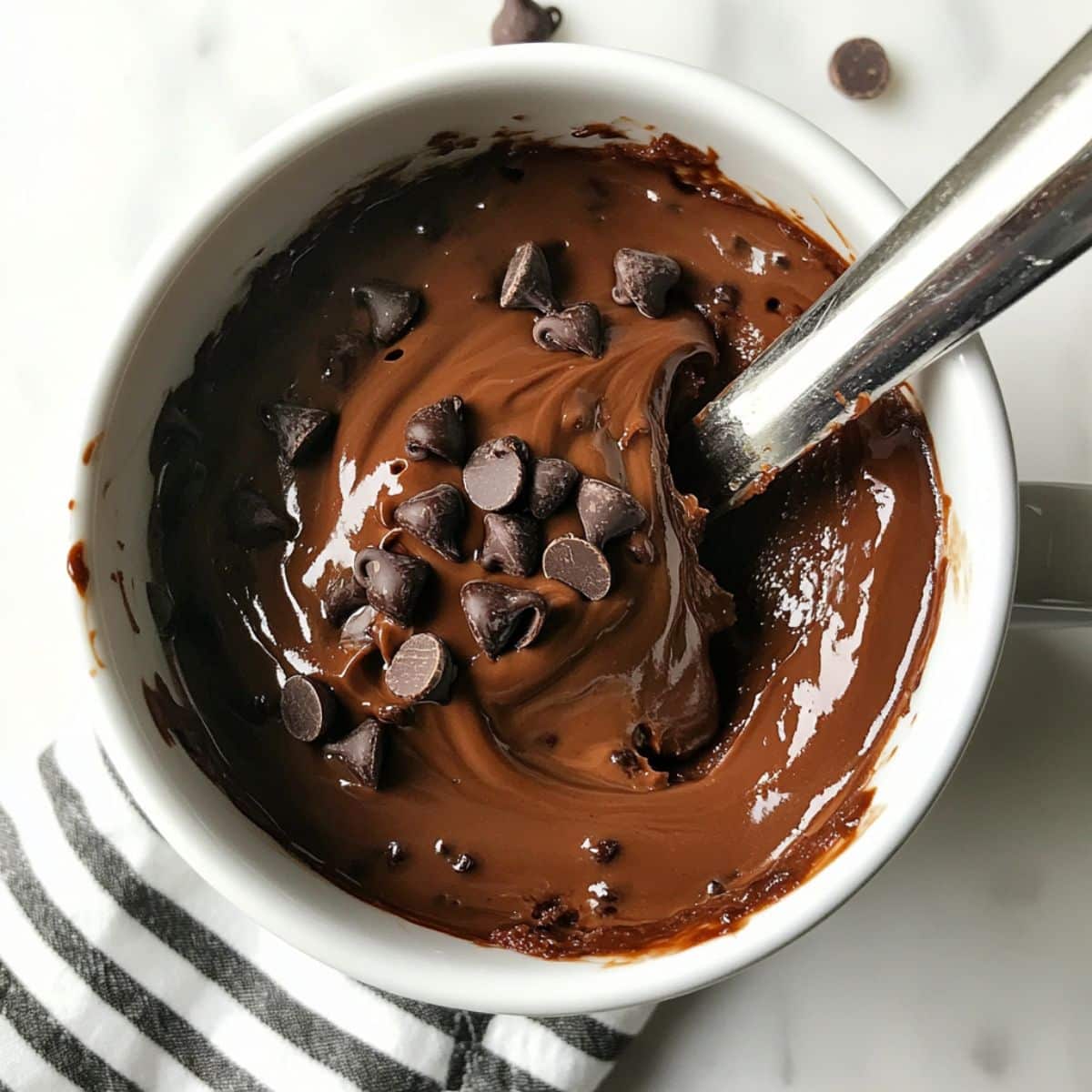 Thick mug cake batter topped with chocolate chips and swirled Nutella, ready to go in the microwave.