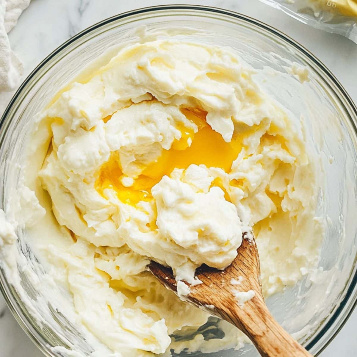 Bowl of mashed egg yolks with mayo and mustard being mixed for deviled eggs. Homemade and mid-prep on a white kitchen counter.