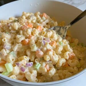 Mixing final Hawaiian macaroni salad with visible creamy mayo, diced veggies, and soft pasta. Step leading to the finished dish.