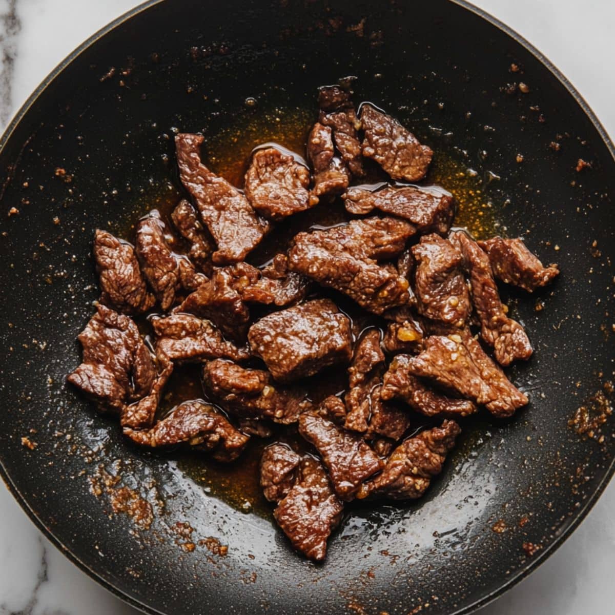 Beef sizzling in oil in a wok, building a golden crust. Crispy edges form the signature Mongolian beef texture.