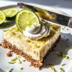 Chilled knife slicing key lime bars on a white kitchen counter. Topped with whipped cream and lime zest.