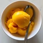Homemade mango sorbet with vibrant color in a bowl, melting slightly. No-churn frozen treat made from real ripe mangoes.