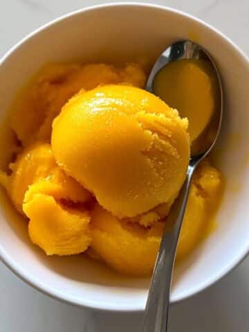 Homemade mango sorbet with vibrant color in a bowl, melting slightly. No-churn frozen treat made from real ripe mangoes.