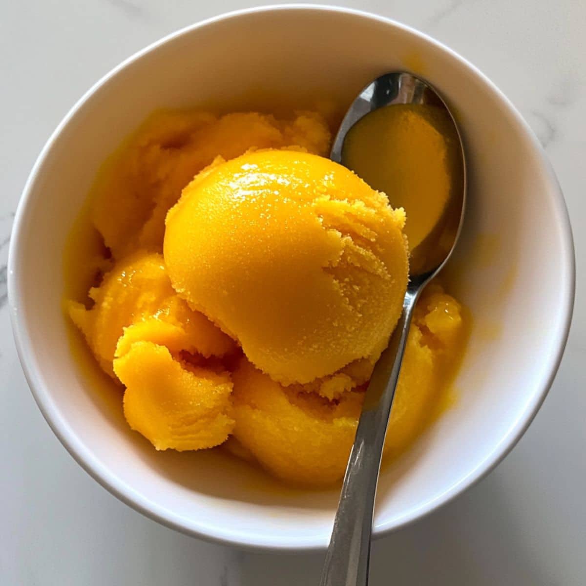 Homemade mango sorbet with vibrant color in a bowl, melting slightly. No-churn frozen treat made from real ripe mangoes.