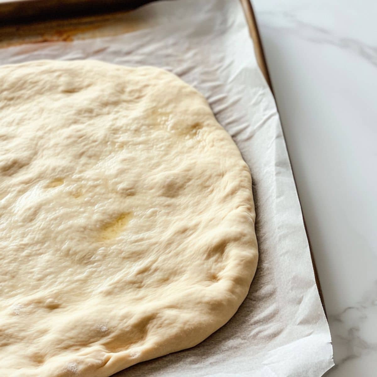 Partially baked breakfast pizza dough on parchment-lined baking sheet ready for toppings.