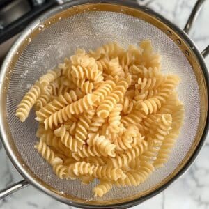 Draining al dente rotini pasta under cold water for Greek salad.